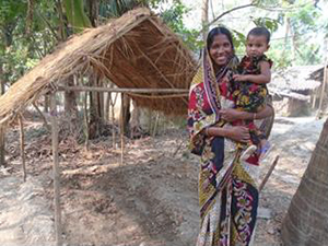Photo of Nasima holding a small child with a village in the background.