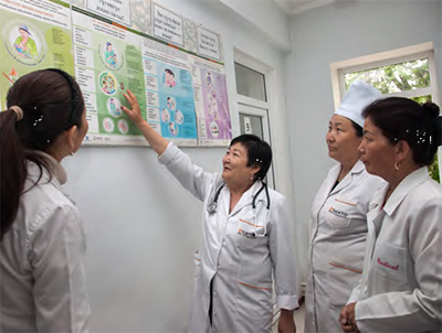 Photo of a group of women in medical coats pointing to charts on a wall.