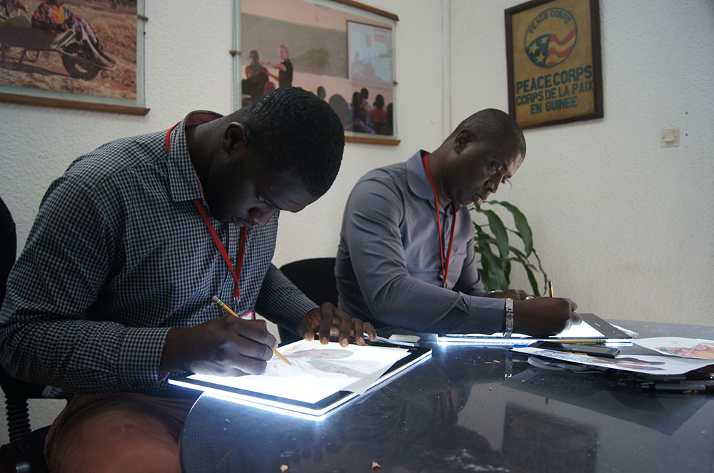 Shekuba Kandeh of HKI Sierra Leone and Ahmed Mansaray of the Sierra Leone Agriculture Research Institute practice line drawings on two light tables.