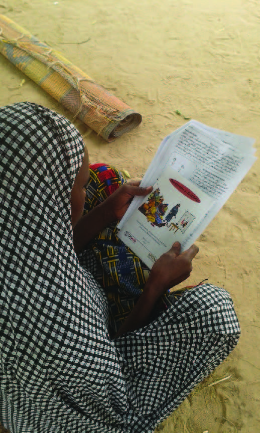 Photo of a woman, sitting on the ground, reading information supplied by the project.