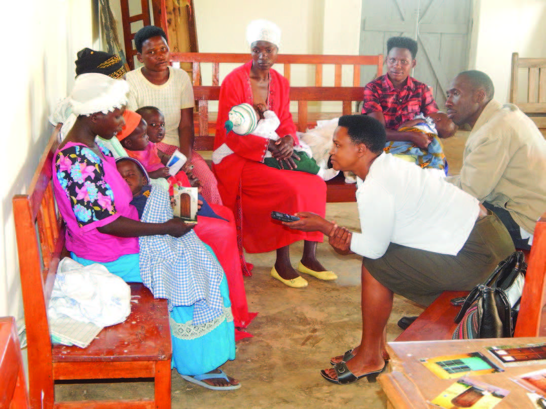 Photo of five women, sitting on benches with their infants, receiving counselling from a woman and a man.