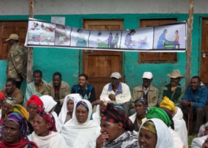 Photo of several people seated outside listening under a banner with medical illustrations.