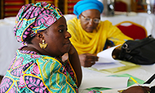 Photo of two women writing notes at a table: The study team presented the implementation process, environmental and contextual factors that enabled and limited success of the Package, outcomes from training health workers and community volunteers in the Package, and impact on maternal knowledge, attitudes, and practices.