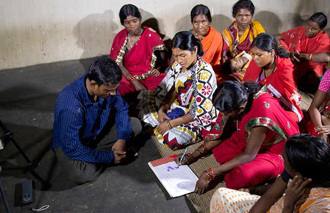 Photo of a man meeting with several women inside, one of whom is writing on a chart