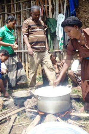 Photo of a man pointing at a large cooking pot outside being stirred by a woman.