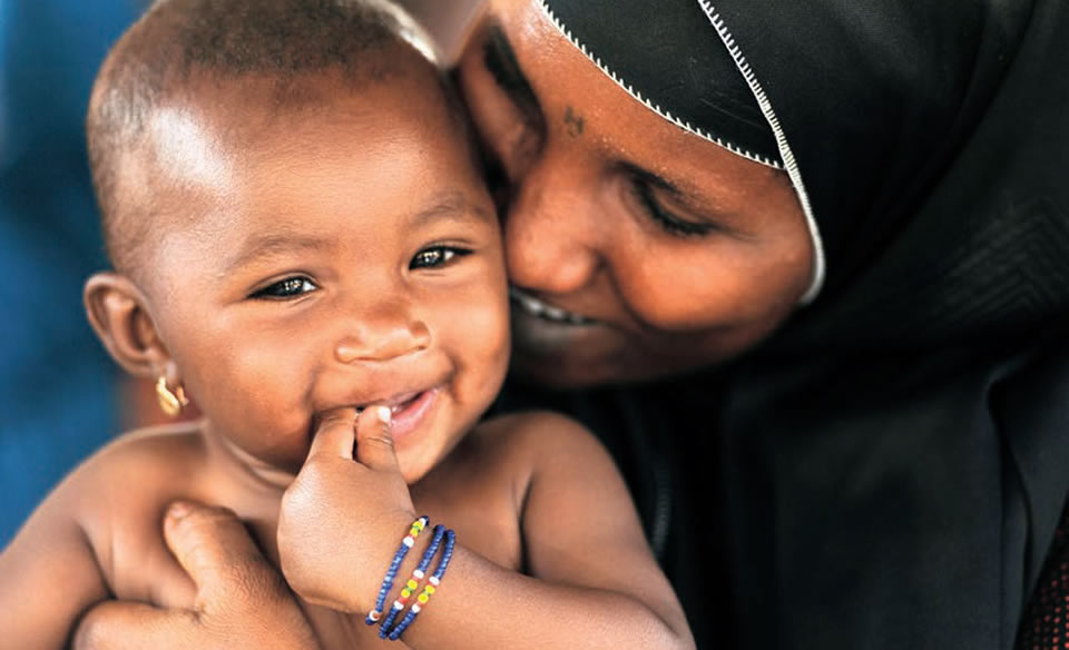 A woman holds her child and they are both smiling.