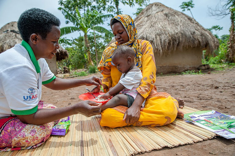 Photo of a mother and child being treated on a mat by a woman in a USAID shirt.