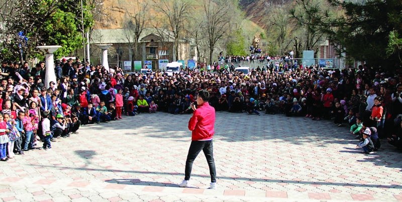 Photo of a man, outdoors, speaking into a microphone to a group of about two hundred people gathered for his talk