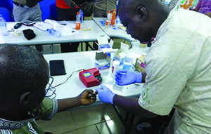 Photo of a health worker taking a blood sample from a patient and testing it with a HemoCue device to diagnose anemia.