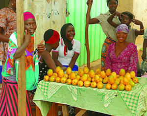 A group of people stand around a table of fruit.