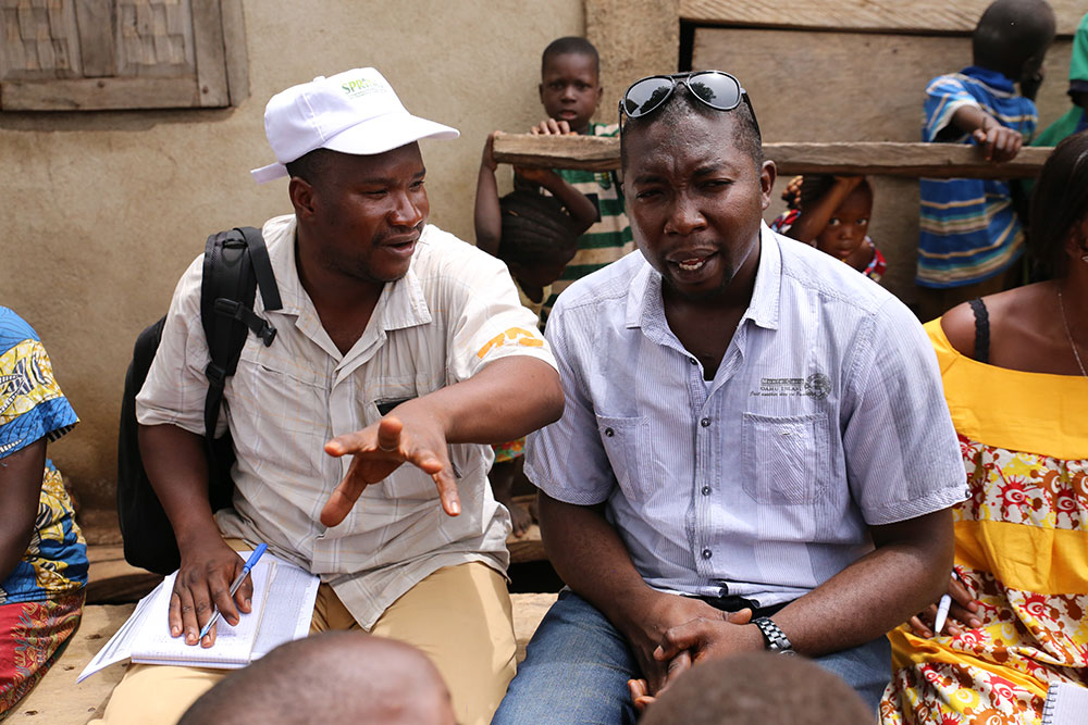 A SPRING/Guinea community extension agent who supports the COCO data collection explains his role to Hamid Turay, SPRING/Sierra Leone Nutrition Coordinator.