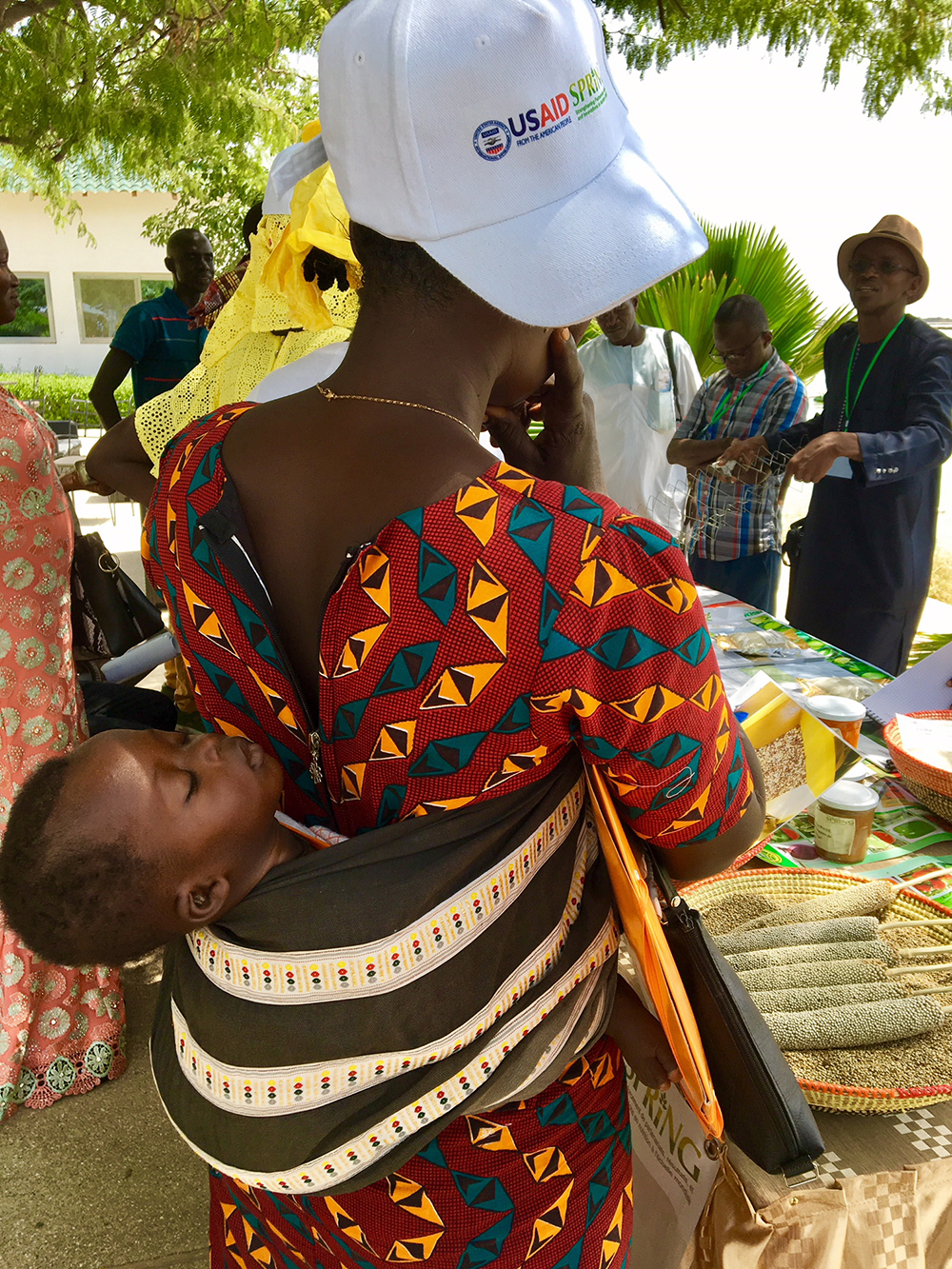 A mother listens to learn more about the project’s achievements with her baby strapped to her back.