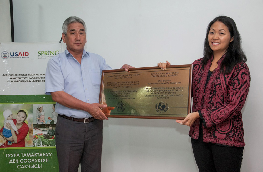 Nora Madrigal, Director of the Health and Education Office, USAID/Kyrgyz Republic, awards a representative from the Shamaldy-Sai General Practice Center with a plaque to certify his health facility as Mother-baby friendly.