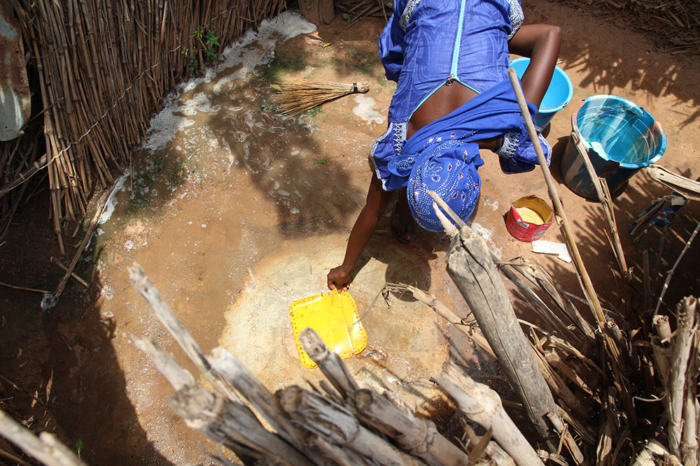 A community member cleans a house-hold latrine and recovers it to prevent flies.