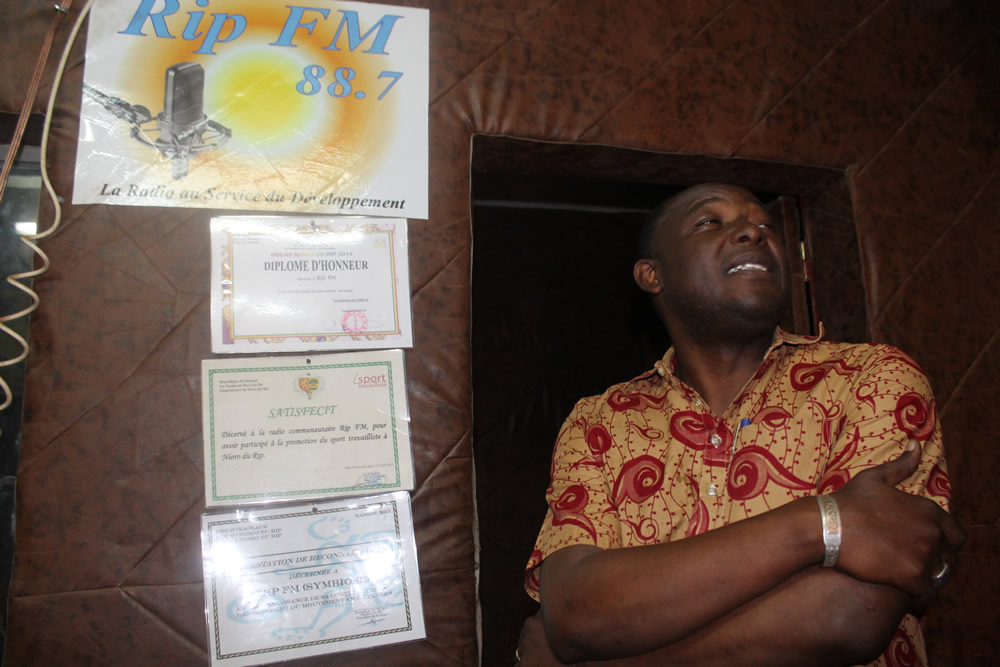RIP FM’s Program Advisor, Leyty Ndiaye, stands next to a display of the community radio’s certificates and awards.