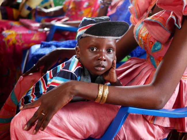 A Senegalese boy resting in his mother's arms as she watches during a community video dissemination event.