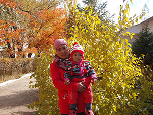 Woman holding baby with fall trees in the background