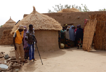 Photo of a video crew filming outdoors among several huts