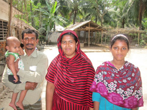 Photo of a mother and father, holding a small infant, and daughter standing outside.