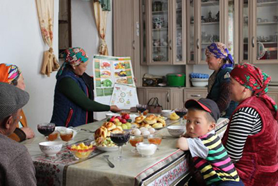 Photo of a family at a table with food, behind the table is a SPRING nutrition poster.