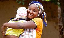 A woman smiles at the camera while holding her baby.
