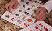 children sit on the floor and look at sheets of paper with images of fruits and vegetables on them