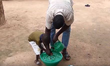 A man and his young son bend over a bowl to wash their hands. The father is teaching the son how.